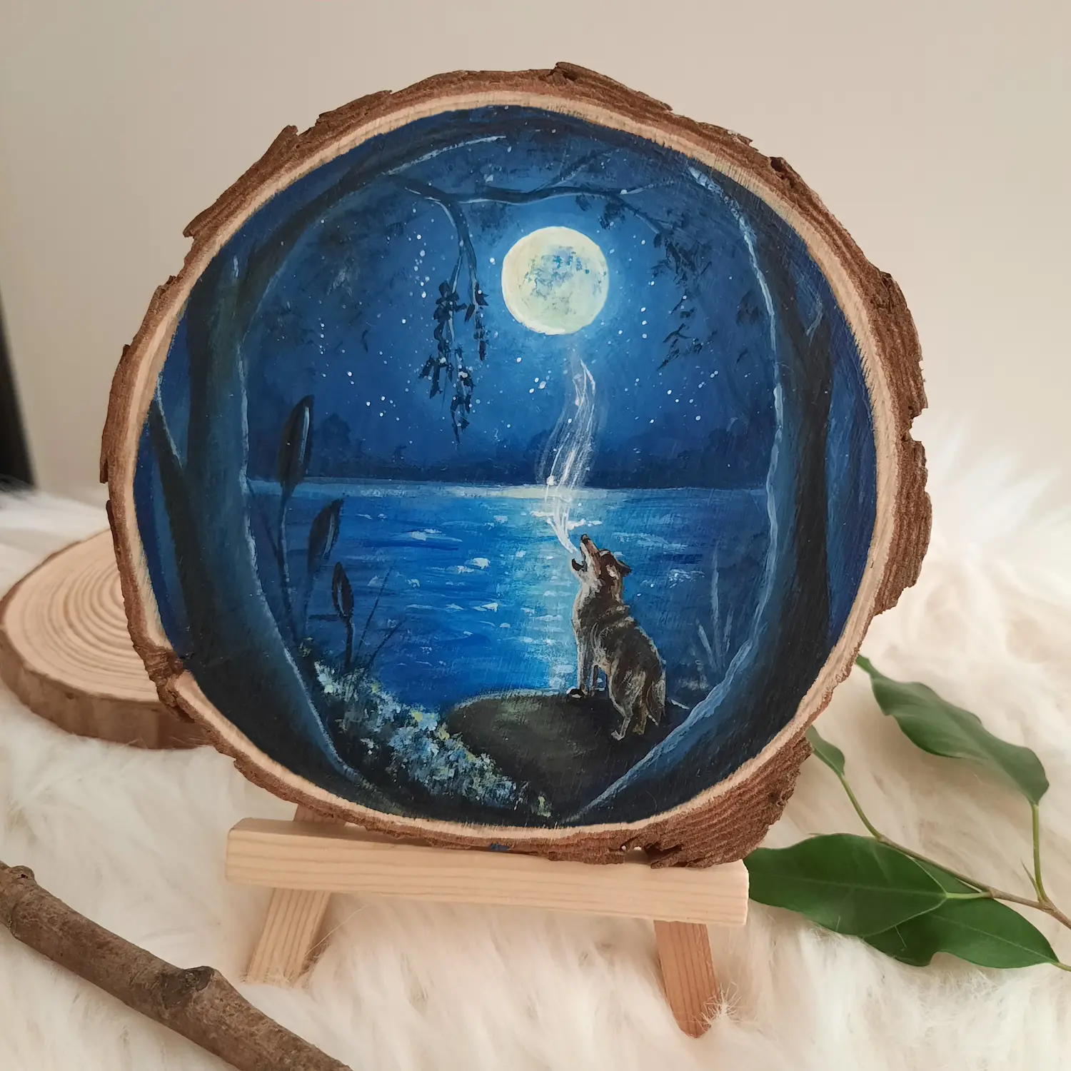 Handgeschilderde boomschijf van huilende wolf aan een blauw meer met volle maan