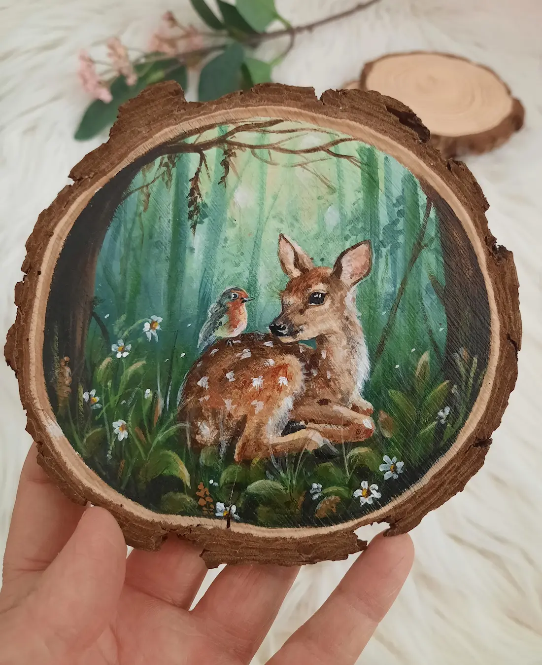 Handgeschilderde boomschijf van een zittende ree met vogeltje op zijn rug in een groen blauw bos
